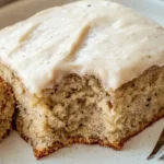 Delicious banana cake with cream cheese frosting on a rustic wooden table.