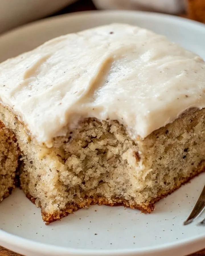 Delicious banana cake with cream cheese frosting on a rustic wooden table.