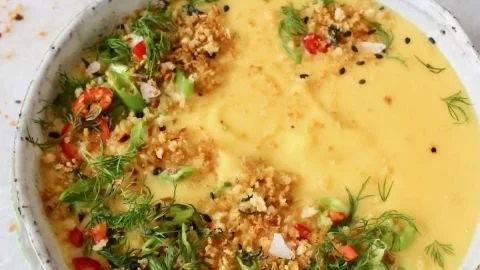 A bowl of creamy cauliflower potato soup topped with fresh herbs.