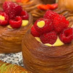 Freshly baked croissant on a wooden table with delicious pastries in the background