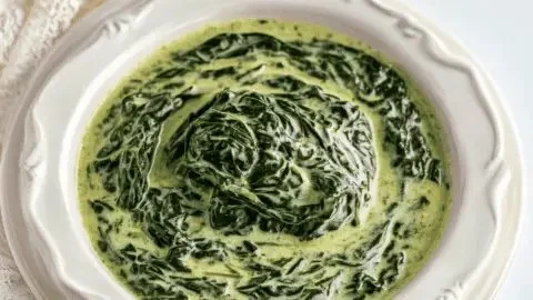 Delicious creamed spinach served in a bowl garnished with spices and cream.
