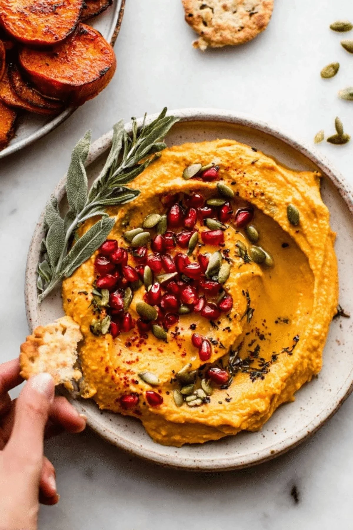 Bowl of creamy pumpkin hummus garnished with herbs and served with fresh vegetables.