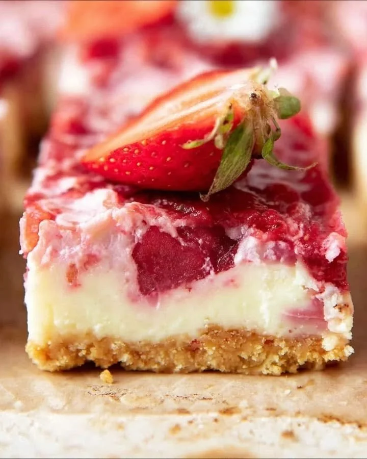 Easy strawberry cheesecake bars topped with fresh strawberries on a white plate.