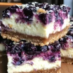 Lemon blueberry cheesecake bars on a white plate, garnished with fresh blueberries.
