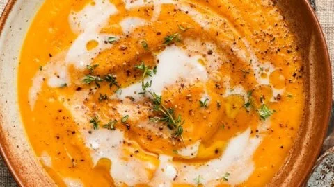 Bowl of creamy roasted butternut squash soup garnished with herbs.