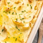 Creamy baked mashed potatoes topped with butter and herbs in a baking dish