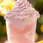 A refreshing glass of whipped pink lemonade with a pink hue and garnished with lemon slices.