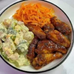 Delicious chicken wings served with potato salad, broccoli, and cauliflower