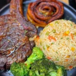 Grilled steak served with fried plantains, vegetable rice, and broccoli