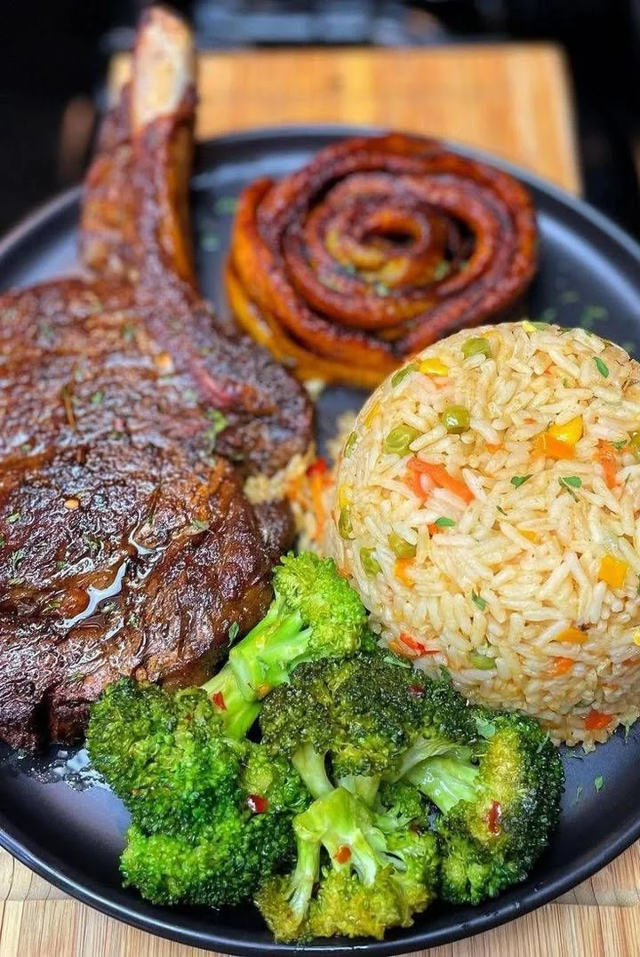 Grilled steak served with fried plantains, vegetable rice, and broccoli
