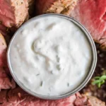 Homemade horseradish sauce in a glass jar with fresh horseradish roots.
