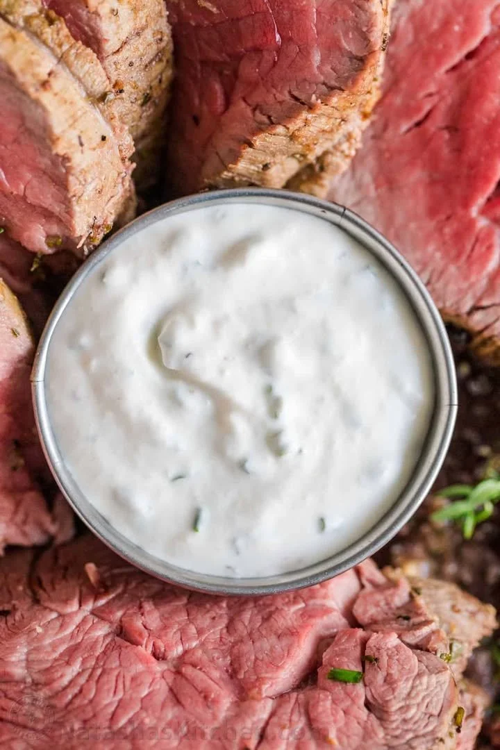 Homemade horseradish sauce in a glass jar with fresh horseradish roots.