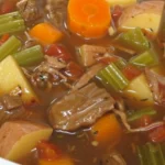 A bowl of old-fashioned beef stew served with vegetables and herbs