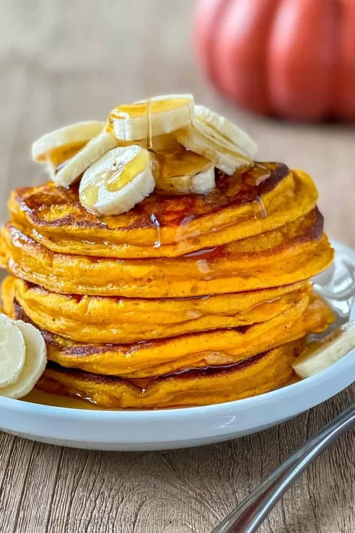 Fluffy pumpkin pancakes stacked with maple syrup and fall spices